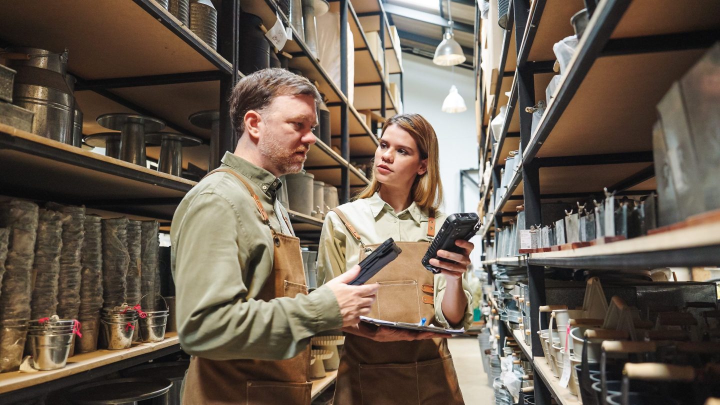 A small business warehouse  worker owner wearing aprons counting  checking stock  management on shelves discussing inventory in a well-organized storage compartment checklist